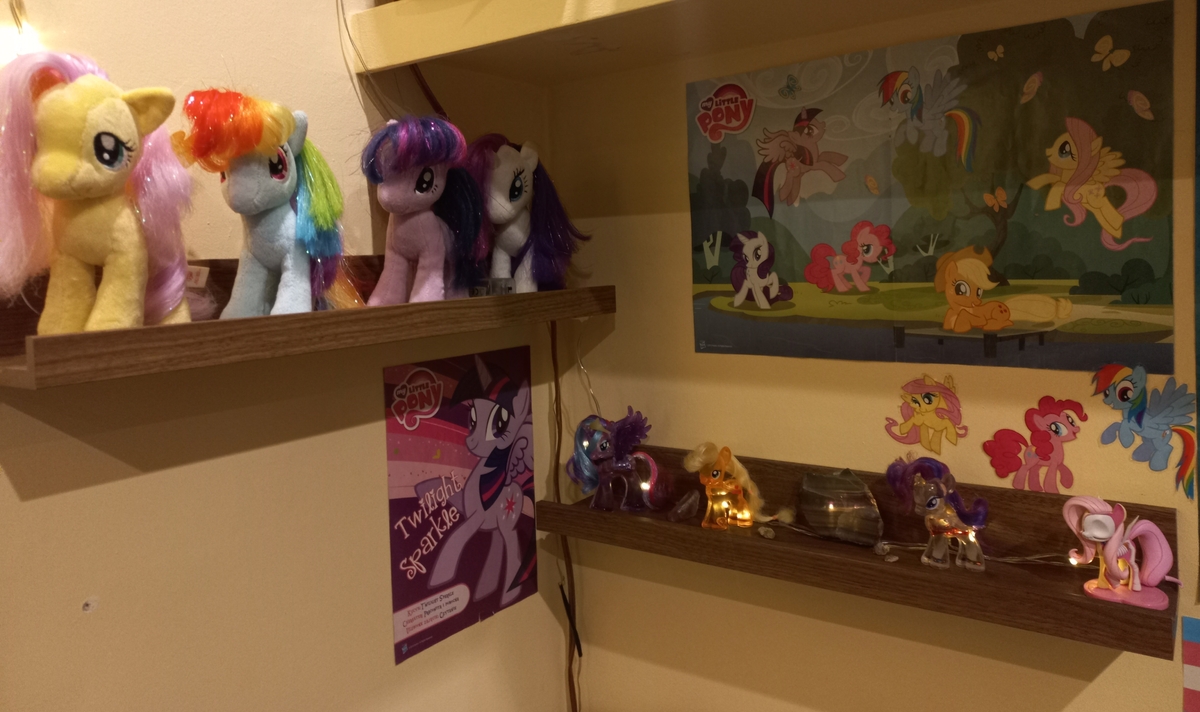 Two shelfes containing various MLP toys like plushies and figurines. Two MLP posters hang behind as well as some stickers.